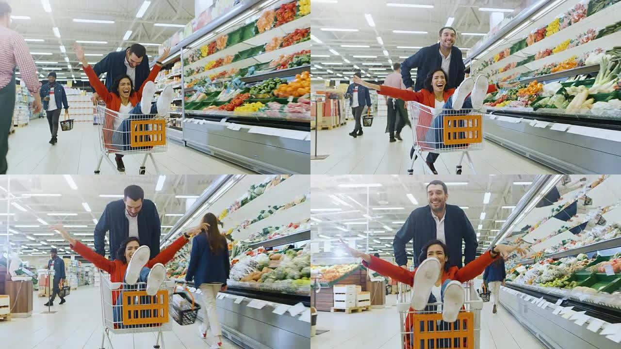 在超市: 男人推着购物车，女人坐在购物车里，幸福的夫妇在手推车里穿过商店的新鲜农产品区玩得很开心。