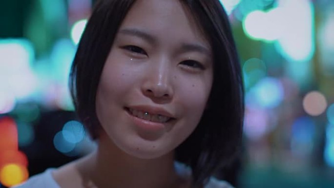 来聚焦美丽的另类东亚女孩微笑的肖像。背景中模糊的大城市灯光发光。