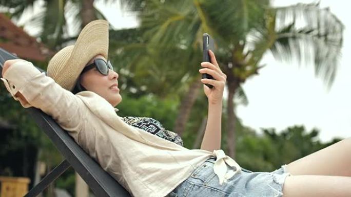 轻松的亚洲年轻女子在沙滩上看手机