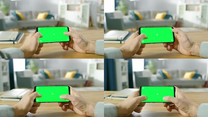 第一人称特写的男子手持绿屏智能手机在横向模式下，用拇指玩游戏。