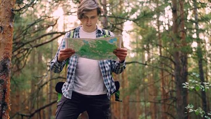 英俊的年轻人旅行者走在森林里，然后站着看地图，寻找正确的道路，然后离开。人，旅行和冒险的概念。