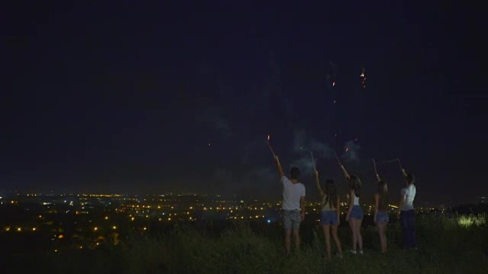 五个人站在城市背景上，用烟花棍站着。夜间