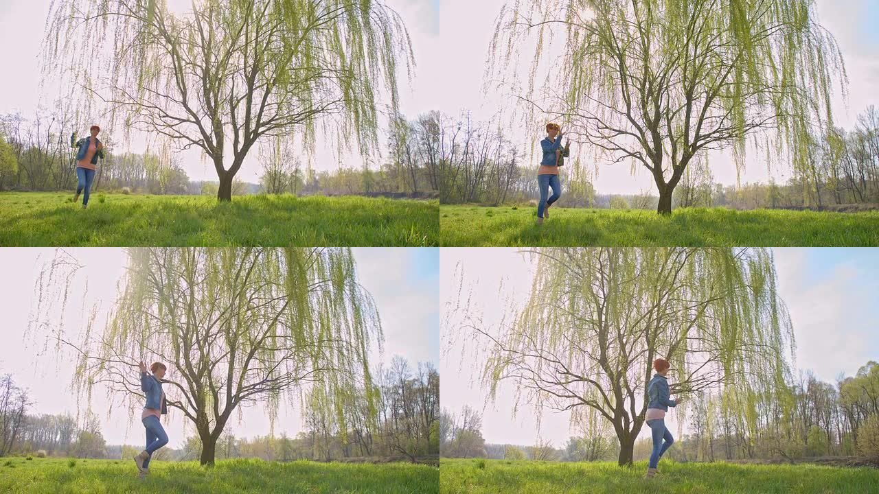 SLO MO快乐的女人在柳树下跳跃