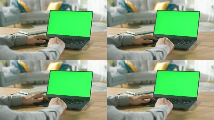 一个男人的特写镜头坐在他舒适的客厅的桌子旁，使用带有绿色模拟屏幕的笔记本电脑。