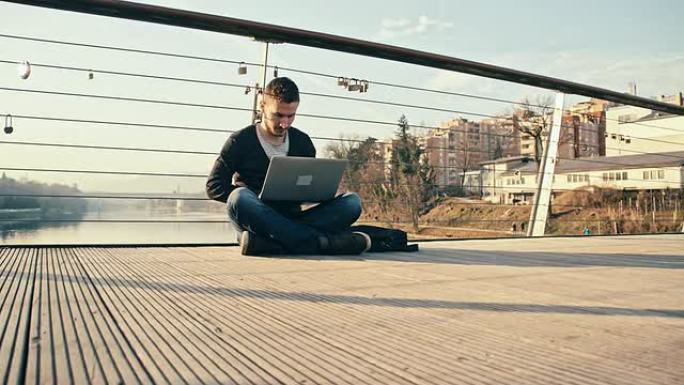 WS男子坐在桥上使用笔记本电脑