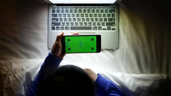 夜间使用水平绿屏智能手机与笔记本电脑的俯视图