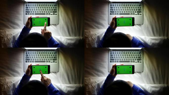 夜间使用水平绿屏智能手机与笔记本电脑的俯视图