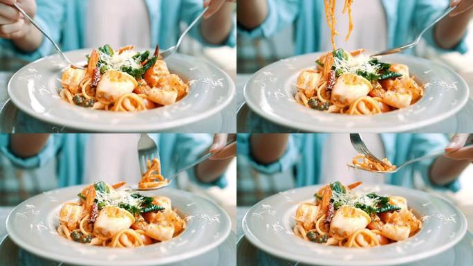 美丽快乐的亚洲女人在餐厅或咖啡馆吃一盘意大利海鲜意大利面，同时微笑着看着食物。