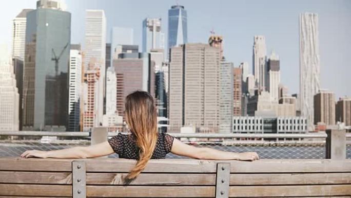 长头发快乐女孩的后视图，坐在长凳上，享受纽约美丽的曼哈顿天际线