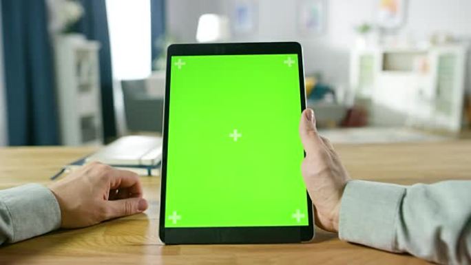 坐在办公桌前的人在肖像模式下使用绿色模拟屏幕数字平板电脑的特写镜头。背景舒适的客厅。