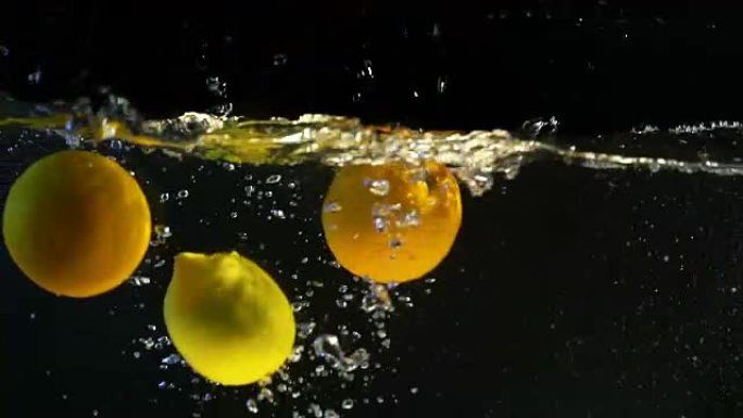 黄色柠檬，橙色，水果落入水中。黑色背景。慢动作