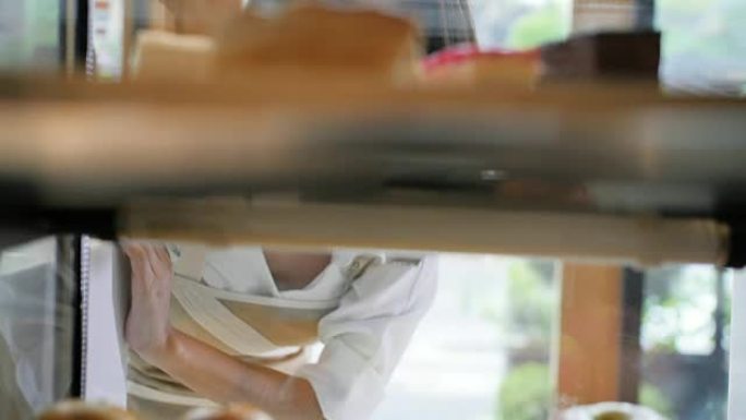 年轻的亚洲妇女透过面包店的窗户看着微笑着看着蛋糕