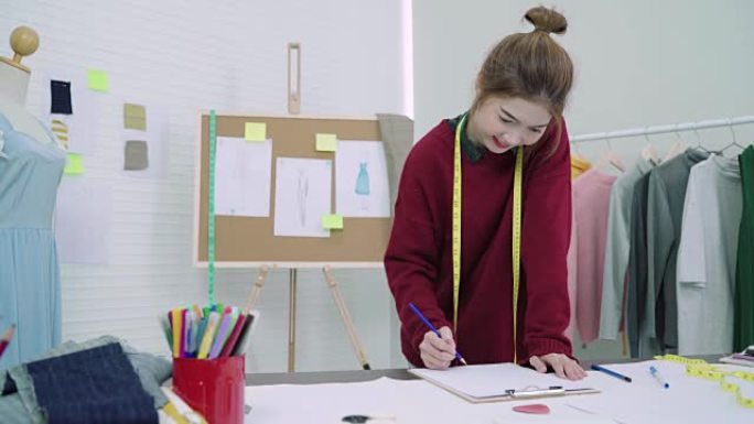 年轻的亚洲女性时装设计师在工作室工作时用铅笔画画，看着纸。