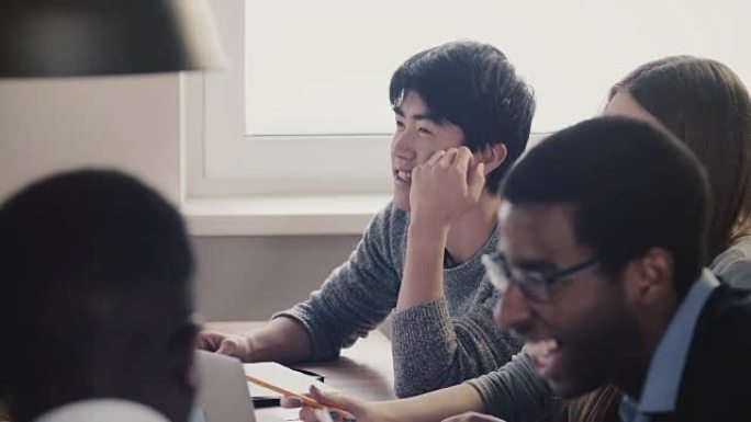 特写快乐的日本年轻员工在多民族办公室会议上与同事一起倾听和大笑