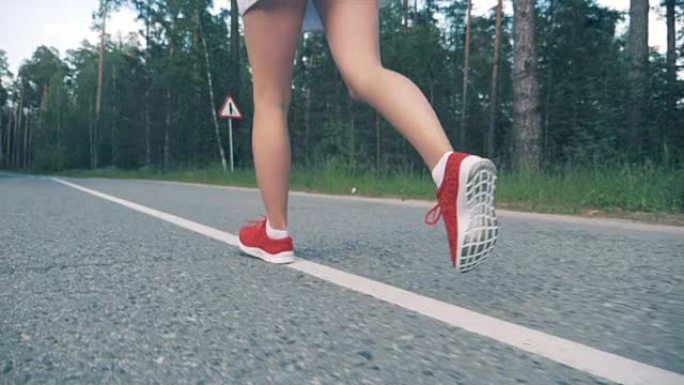 穿着运动鞋的年轻女士正在慢动作地沿着森林公园奔跑。女运动员慢跑。