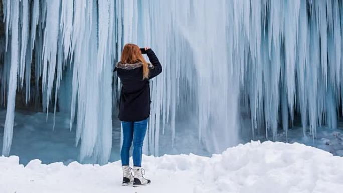 年轻女子在冬天为瀑布拍照