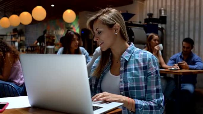 自信的女人在咖啡店里用笔记本电脑工作，同时享受美味的咖啡