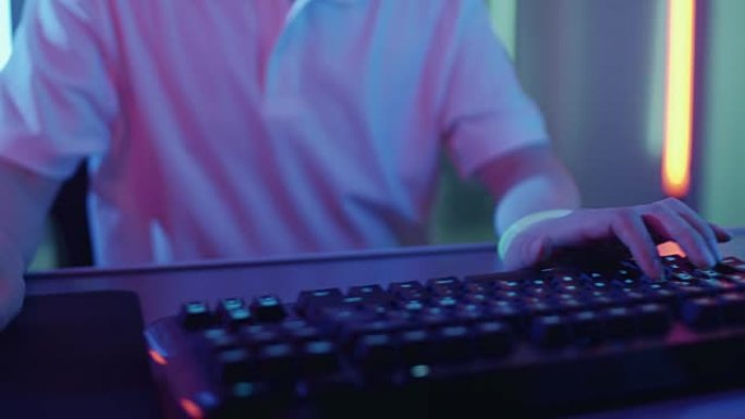 游戏玩家在键盘上玩视频游戏并使用鼠标的手的特写镜头。时尚的街机霓虹灯亮红色，粉红色，紫色，绿色。