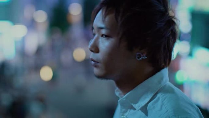 英俊的日本年轻人看着大城市的灯光的肖像。在后台，大城市的广告广告牌灯光在夜晚发光。