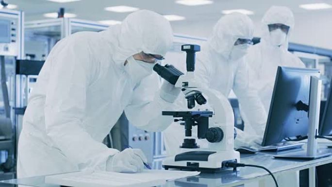 在实验室中，穿着防护服的科学家进行研究，使用显微镜并将数据输入个人计算机。生产半导体和药品的现代工厂