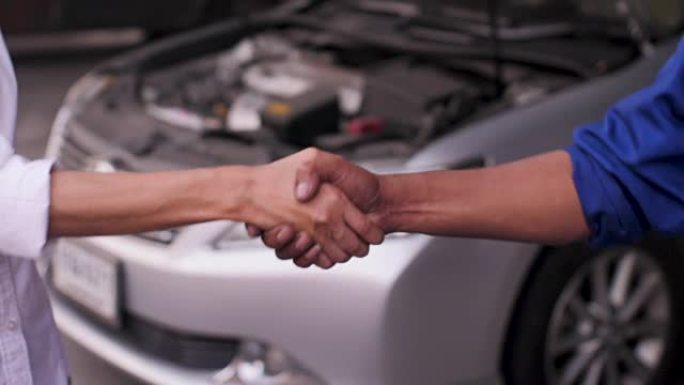 在汽车维修店，汽车服务概念中，机械师和客户握手的特写镜头