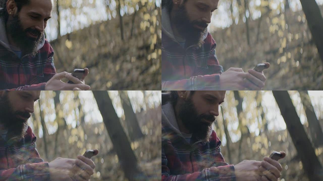 微笑的男人在森林中的智能手机上发短信