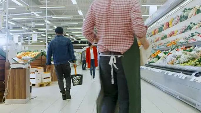 在超市: 幸福的三口之家牵着手走过商店的新鲜农产品区。父亲推着购物车，母女牵着手，玩得开心。