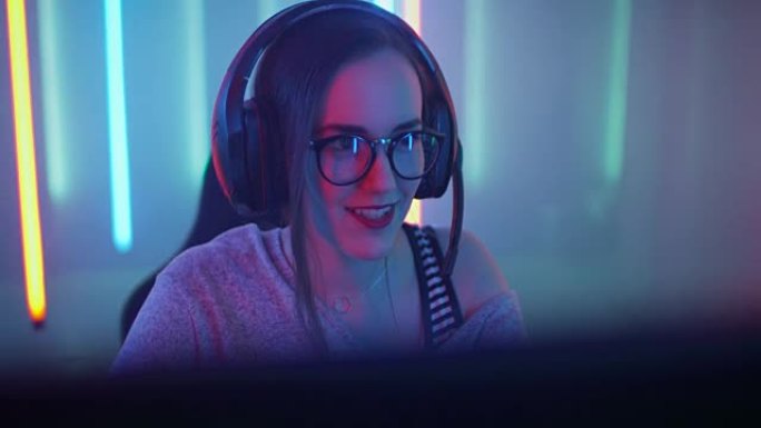 美丽的职业玩家女孩坐下来在她的个人电脑上玩在线视频游戏。戴着眼镜对着麦克风说话的休闲可爱怪胎。网络体