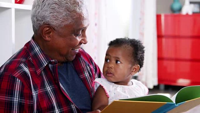 祖父坐在家里和小孙女一起看书 -- 慢动作拍摄
