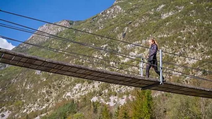 年轻女子在山腰穿过一座木制吊桥