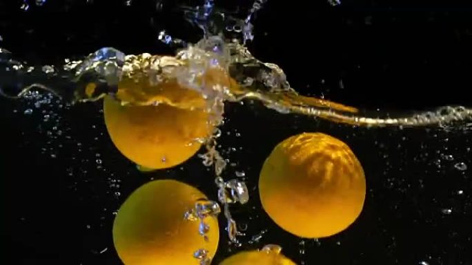 橙色带着气泡掉入水中的慢动作视频。孤立的黑色背景上的水果。