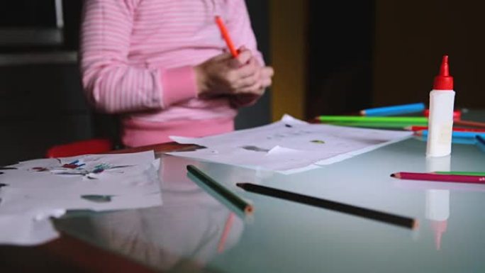 相机向右滑动，显示穿着粉红色毛衣的欧洲小女孩拿着铅笔在桌子上用文具画画