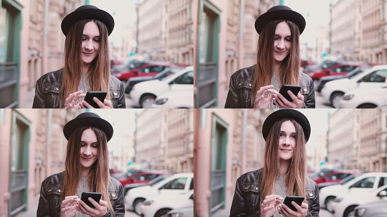 戴着时尚帽子微笑的年轻欧洲女性带着智能手机走在城市街道上，向前看慢动作