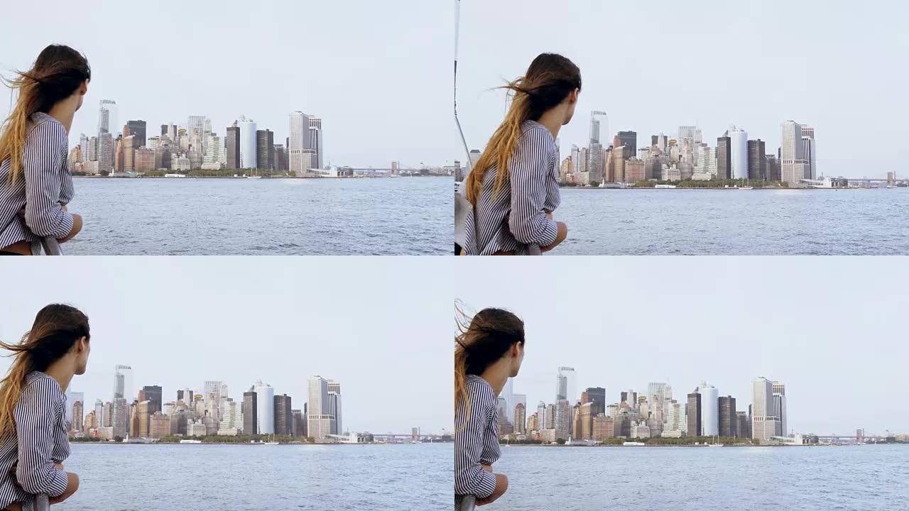 快乐微笑的欧洲女人，留着飞舞的头发，从一艘旅游船上欣赏纽约著名的曼哈顿天际线景色