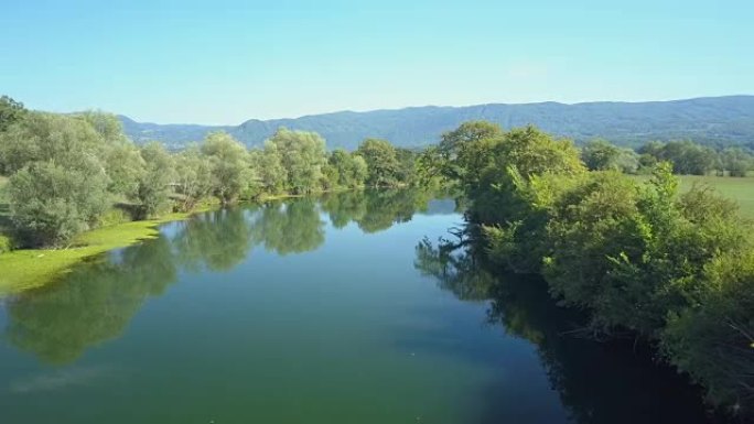 空中: 沿着一条仍然深蓝色的河流飞过，穿过乡村景观。