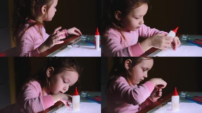 穿着粉色毛衣的美丽的小学龄前欧洲女孩孩子的特写镜头坐在桌子旁边，涂纸形状