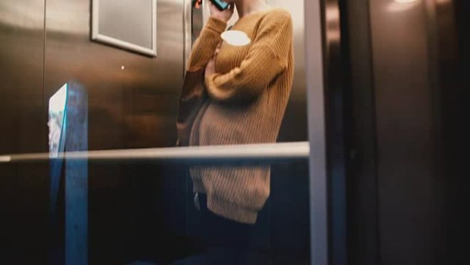 年轻放松的欧洲妇女在透明的玻璃墙电梯里骑着电话聊天，微笑着