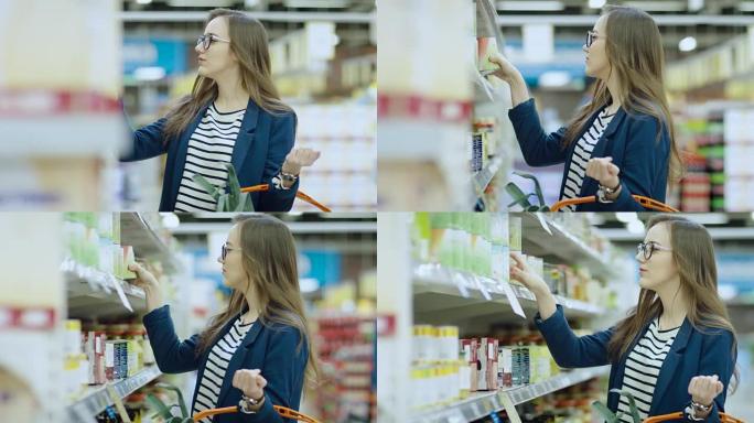 在超级市场:美丽的年轻女子浏览在商店的罐头食品部分。她的购物篮里装满了健康食品。