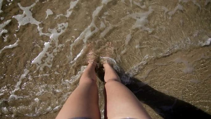 沙滩上年轻女子的腿，海浪冲刷着