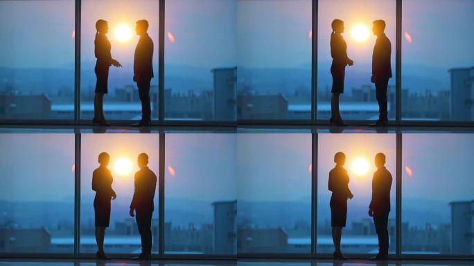 男人和一个女人在日出背景的全景窗户附近聊天