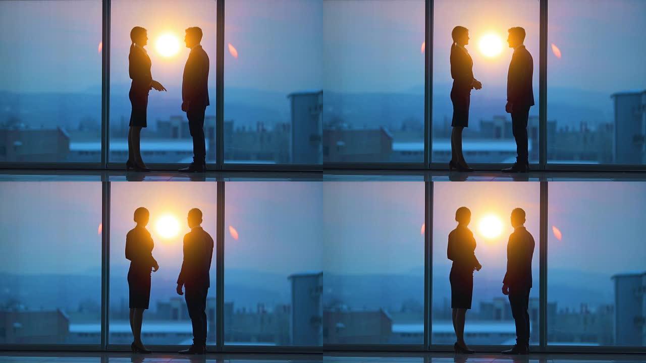 男人和一个女人在日出背景的全景窗户附近聊天