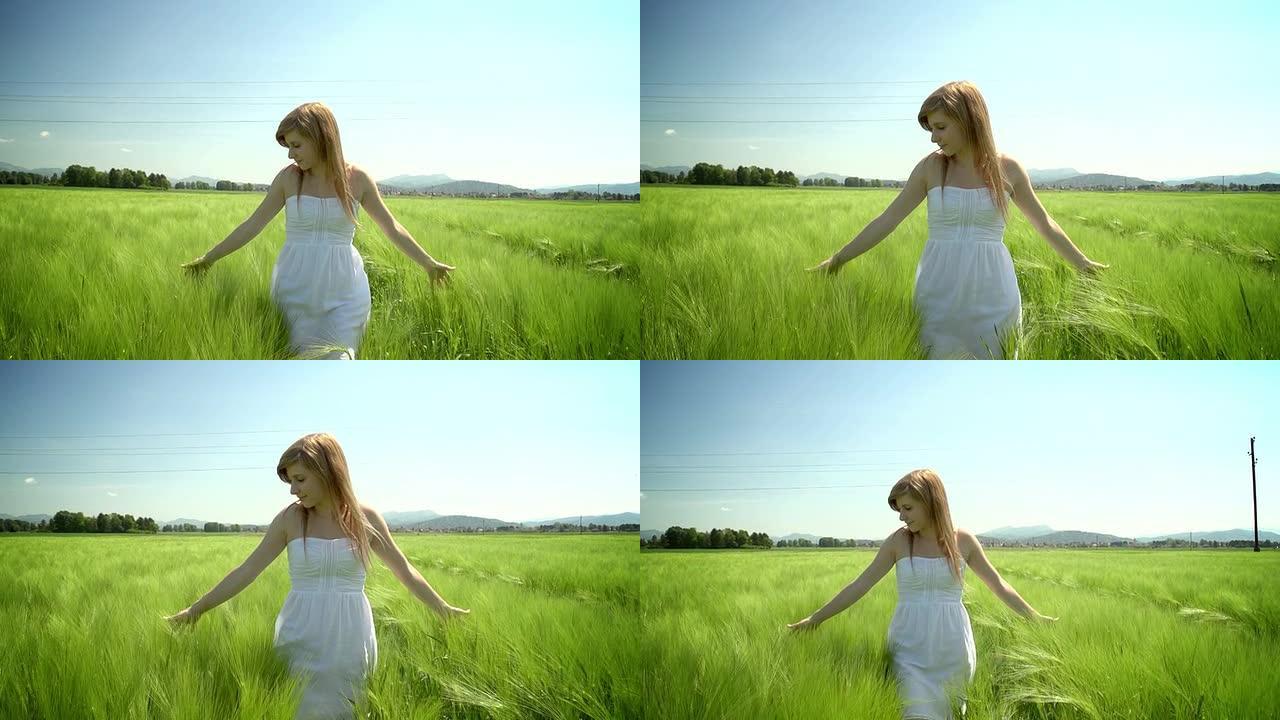 身穿白色连衣裙的年轻女子穿过绿色的麦田