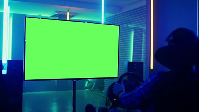 专业玩家坐在赛车座椅模拟器驾驶舱的绿色模拟屏幕电视前，方向盘和玩赛车在线视频游戏。