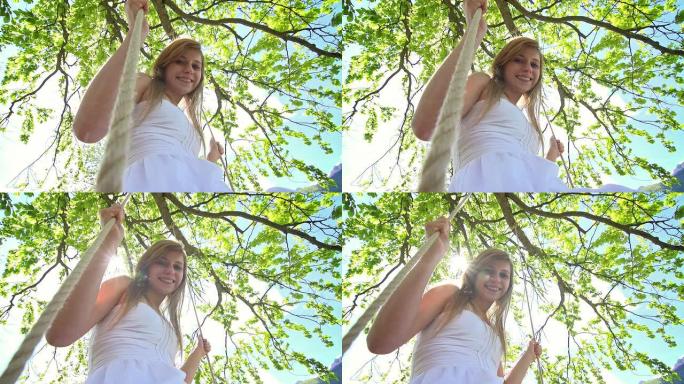 一个穿着白色连衣裙的女孩在树下用绳子荡秋千