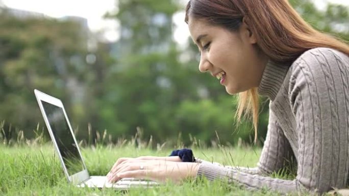 年轻女子在公园户外在笔记本电脑键盘上打字