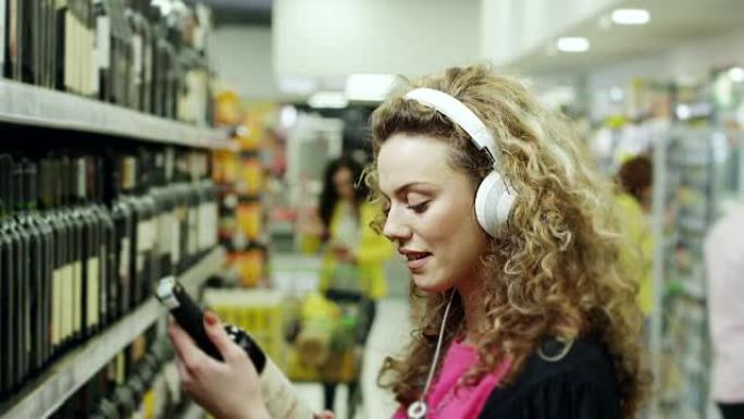 妇女在超市选择一瓶葡萄酒并在耳机上听音乐