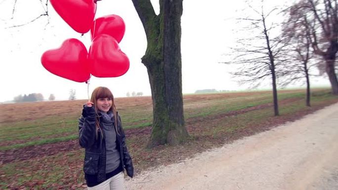 带着红色心形气球的女孩在公园里等待