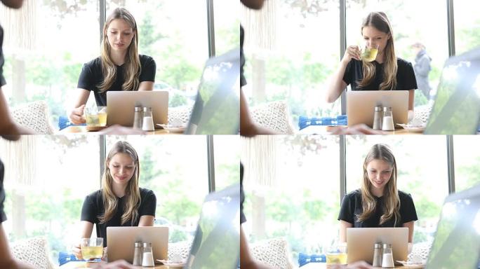 女人在咖啡馆使用笔记本电脑时喝绿茶