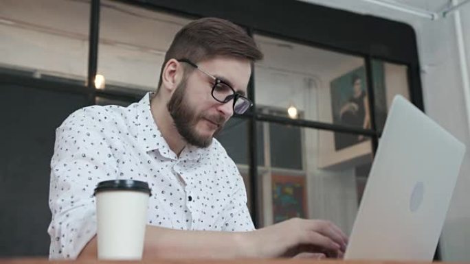 男子在笔记本电脑键盘上打字并喝咖啡