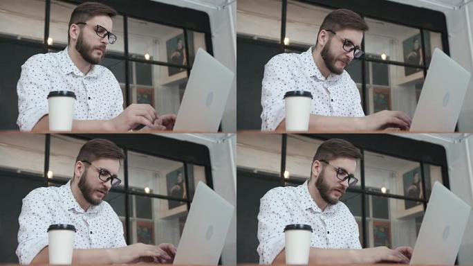 男子在笔记本电脑键盘上打字并喝咖啡